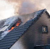 fragment of a sooty white brick home that is on fire with flames and picture